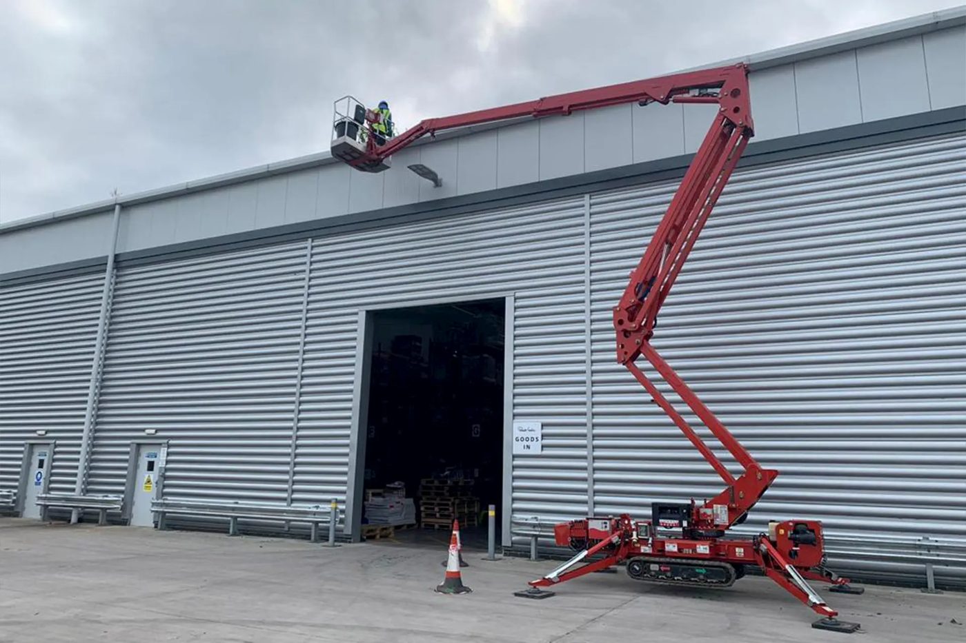 Worker in a raised cherry picker basket cleaning commercial guttering